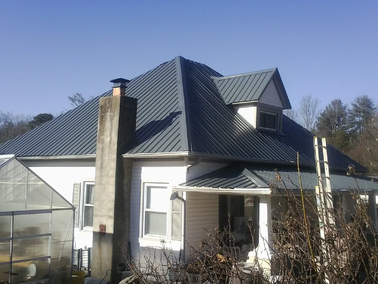 Dark blue standing seam metal roof on a white farmhouse with dormer — Slate & Tile Roof Repair by Roofing Brothers in Franksville