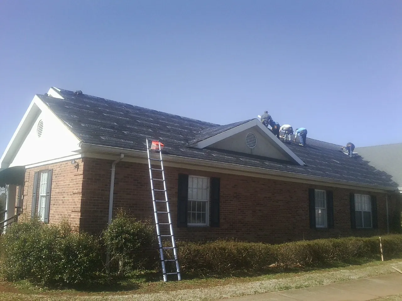 Crew tearing shingles off a brick ranch roof with a ladder set — Metal Roof Repair work by our crew in Franksville