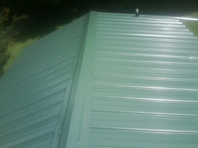 New green metal panels meeting at the ridge of a roof — Flat Roof Repair work by our crew in Franksville