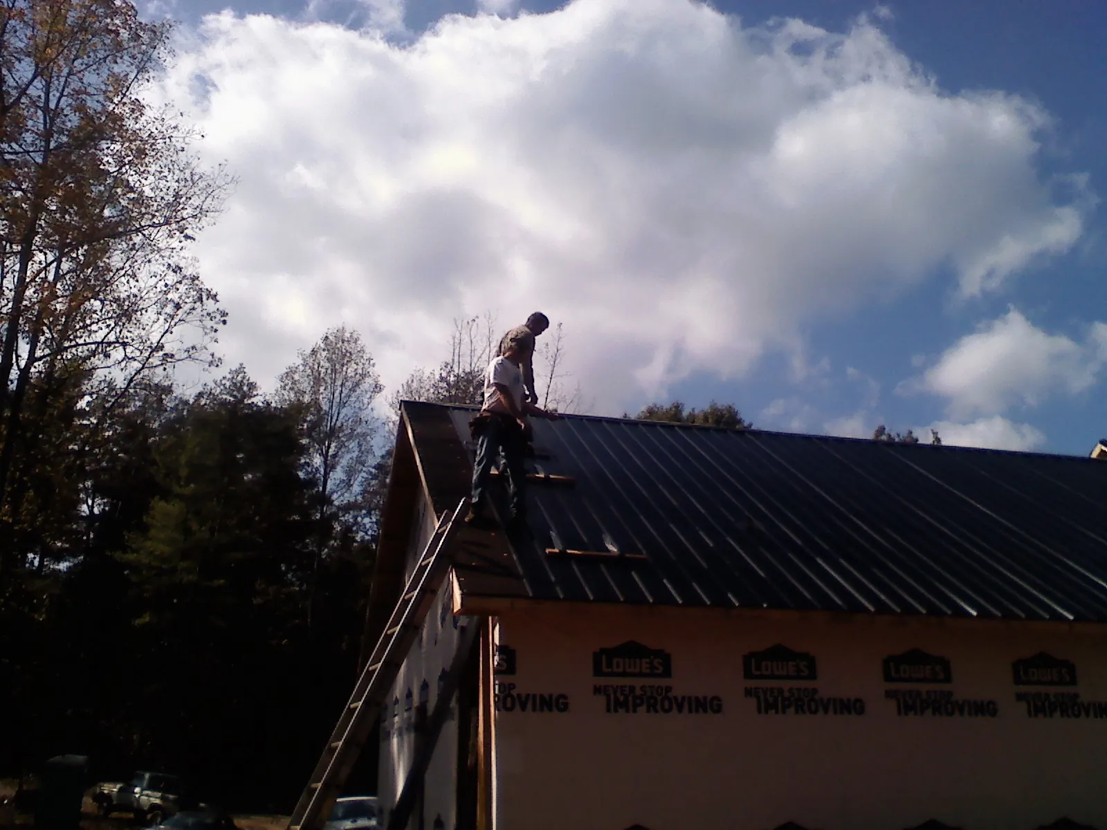 Roofer fastening dark metal panels high against a cloudy sky, from a Roof Inspection job in Franksville