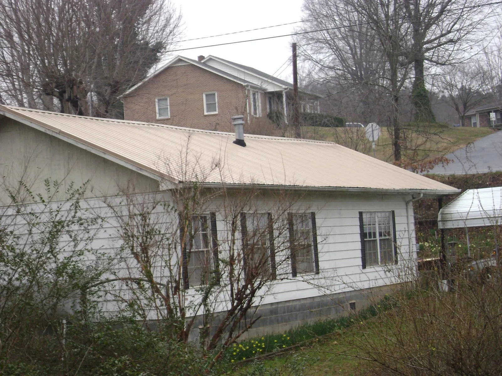 Tan metal roof on a white sided house set into a hillside — Commercial Roofing by Roofing Brothers in Franksville